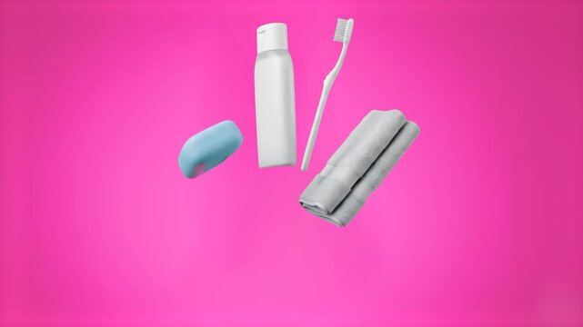 A set of personal hygiene and skincare essentials including a bottle, toothbrush, soap bar, case, and rolled towel levitates against a vibrant magenta pink backdrop. Great for personal care marketing,