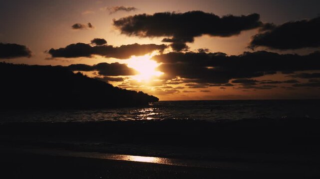 朝日に照らされる美しい波打ち際とシルエットの島影（スローモーション）