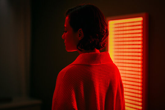 Rear view silhouette of person in waffle robe standing in front of red light therapy panel