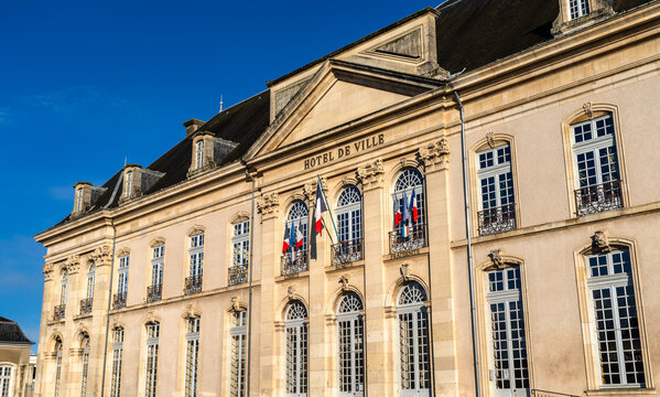 The exterior of the City Hall of Toul in France featuring classical architecture and French flags against a blue sky.