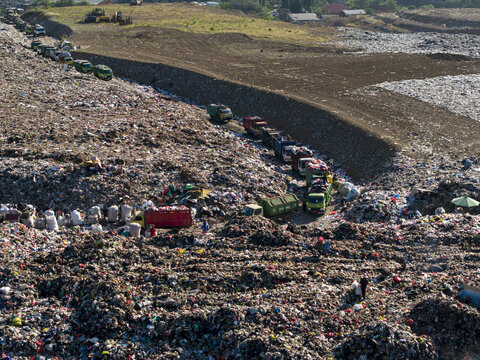Aerial view of TPA Suwung landfill with waste trucks and workers sorting through piles of trash in Kecamatan Denpasar Selatan, Bali, Indonesia.