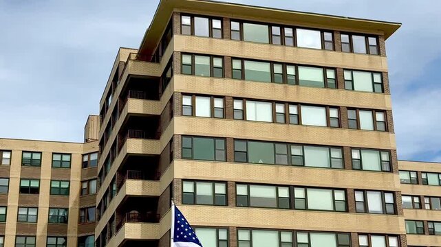 Tilt down view of an American flag waving in the wind with a large apartment building in the background
