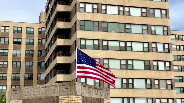 Tilt up view of an American flag waving in the wind with a large apartment building in the background