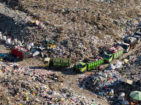 Aerial view of TPA Suwung landfill with garbage trucks collecting waste and workers sorting through piles of trash in Kecamatan Denpasar Selatan, Bali, Indonesia.
