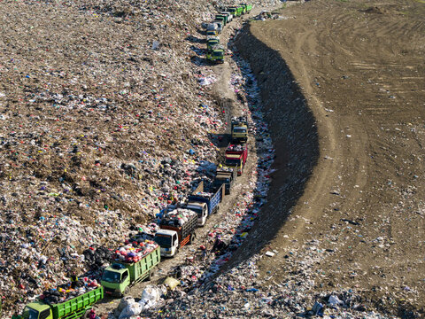 Aerial view of TPA Suwung landfill with a long line of waste collection trucks navigating through piles of garbage in Kecamatan Denpasar Selatan, Bali, Indonesia.