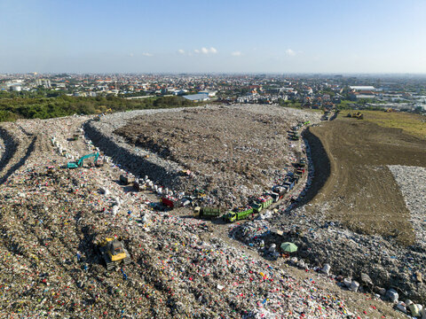 Aerial view of TPA Suwung landfill with waste piles, heavy machinery, and trucks in Kecamatan Denpasar Selatan, Bali, Indonesia.
