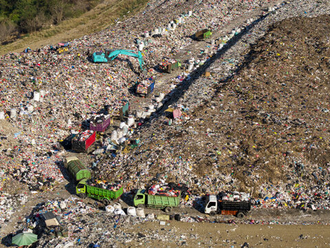 Aerial view of TPA Suwung landfill with excavators and trucks sorting waste in Kecamatan Denpasar Selatan, Bali, Indonesia.