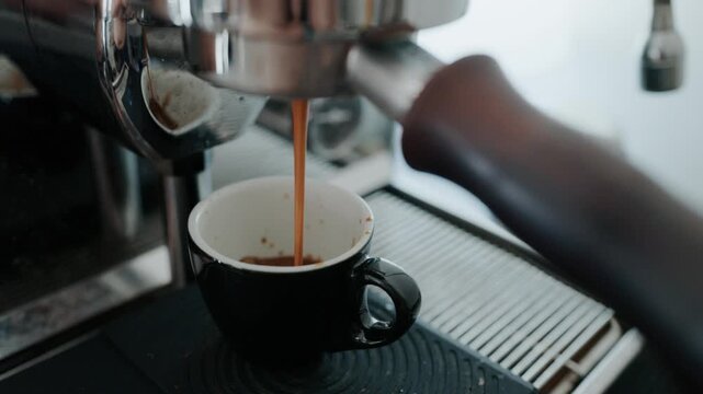 4K Pouring coffee stream from professional machine in cup. Barista man making double espresso, using filter holder. Flowing fresh ground coffee. Drinking roasted black coffee in the morning.