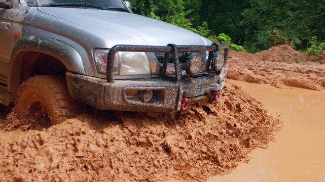 Close up of 4x4 SUV tire spinning in deep mud with heavy splash. Cinematic 4K slowmo video showing engine power and wheel traction.
