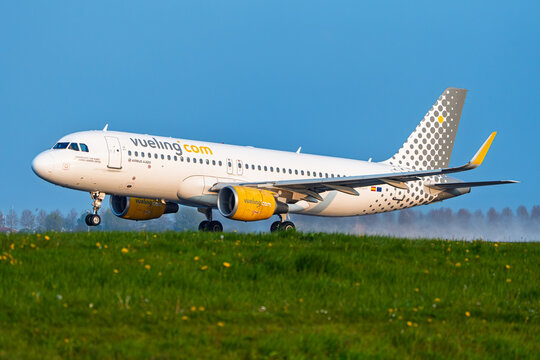 Amsterdam, Netherlands, 21.04.2023 - A Vueling Airlines Airbus A320 passenger aircraft landing on the runway at Schiphol Airport, seen from a grassy field during a sunny.