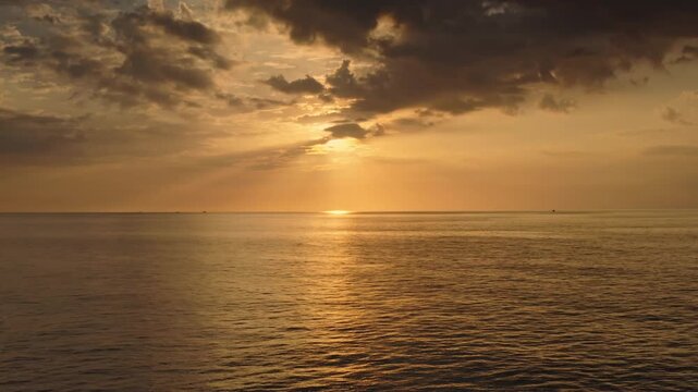 Tranquil Phuket island sunset, golden light reflecting on calm ocean waters under a cloudy dramatic sky, creating a serene and warm tropical seascape. Natural background, amazing evening panorama