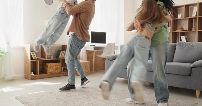 Happy family parents and children dancing at home. Mother and father lift and spin kids in cozy living room, laughing in denim and sharing fun. Celebrates joyful family bonding together.