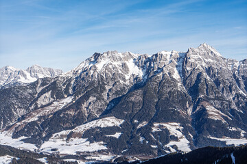 Naklejka premium A breathtaking panoramic view of majestic snow-covered Alpine mountain peaks in Saalbach Hinterglemm, Austria, captured on a clear sunny day during the peak winter ski season.