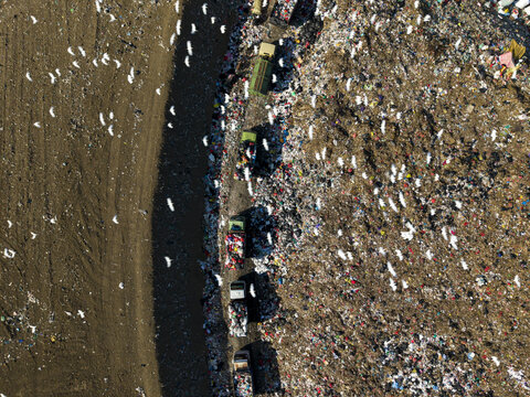 Aerial view of TPA Suwung landfill with waste collection trucks on a path surrounded by piles of refuse and flocks of white birds in Kecamatan Denpasar Selatan, Bali, Indonesia.