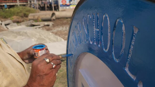 Indian stone sculpture artist hand-painting a Platinum Jubilee commemorative school logo sculpture in Odisha, India. Traditional artisan craftsmanship and sculpture finishing process