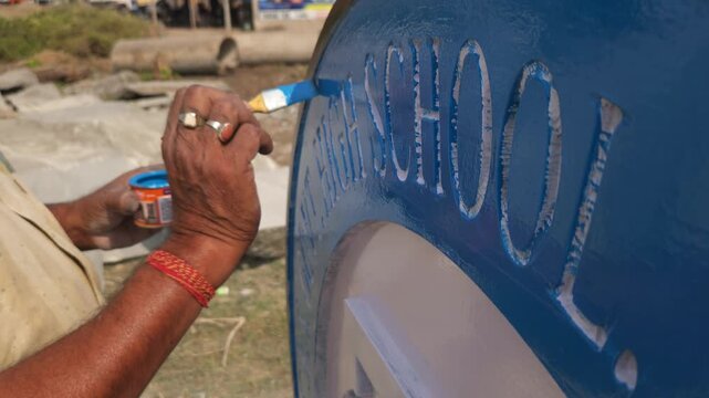 Authentic footage of an Indian stone sculpture artist hand-painting a Platinum Jubilee commemorative school logo sculpture in Odisha, India. The video showcases traditional craftsmanship
