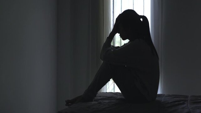 Backlit silhouette of sad lonely woman crying in dark house. Concept of mental illness, sadness, despair, and emotional stress.