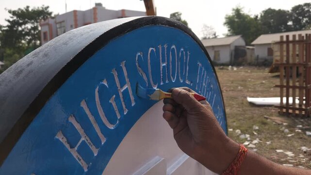 Indian stone sculpture artist hand-painting a Platinum Jubilee commemorative school logo sculpture in Odisha, India. Traditional artisan craftsmanship and sculpture finishing process