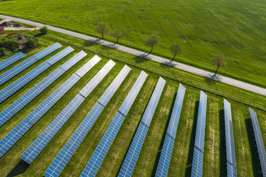 Aerial view of a solar farm with rows of photovoltaic panels installed on a green field next to a rural road in Kunkovice, Zlin Region, Czechia.