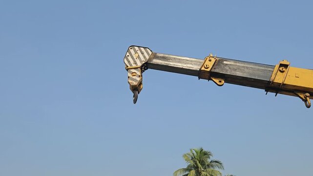 Mobile crane boom with heavy-duty lifting hook suspended against clear blue sky. Industrial lifting equipment, engineering machinery, infrastructure development, heavy construction