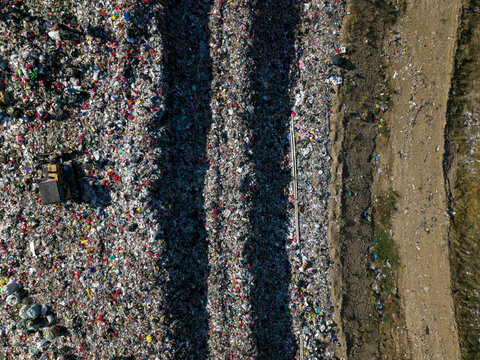 Aerial view of TPA Suwung landfill showing massive piles of waste, heavy machinery, and dirt paths in Kecamatan Denpasar Selatan, Bali, Indonesia.