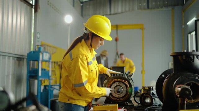 Caucasian female industrial engineer in yellow uniform and hard hat inspecting large electric motor during maintenance work in manufacturing factory workshop. Professional technician testing machinery