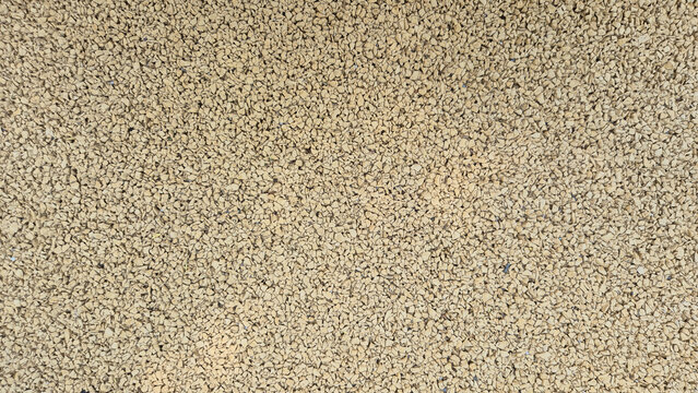 A close-up view showing a dense, textured background composed of small, beige or light brown rubber granules tightly packed together on a flat surface.