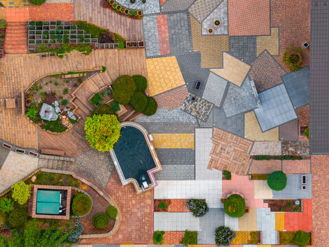 Aerial view of a landscaped garden featuring various paving patterns, stone tiles, a small pond, and manicured shrubs in Otnice, South Moravian Region, Czechia.