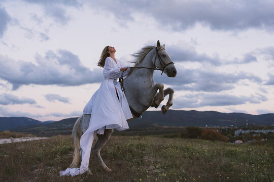 Woman horse rearing majestic white steed against dramatic cloudy sky at sunset