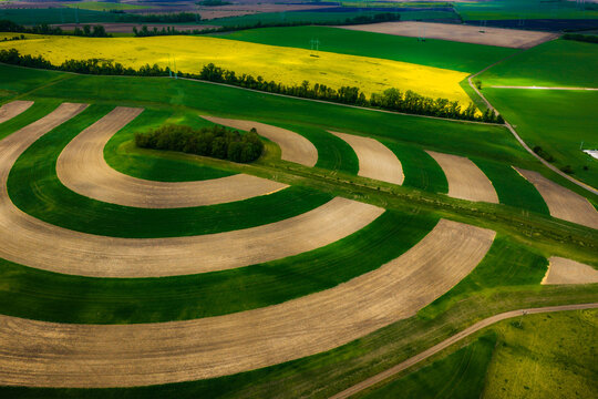 Aerial view of agricultural fields with contour plowing patterns and a small patch of trees in Otnice, South Moravian Region, Czechia.
