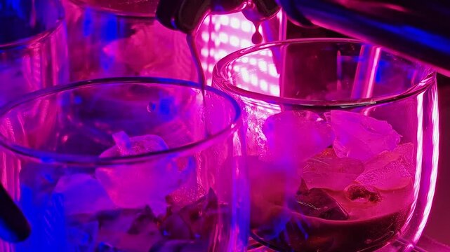 A sleek dark coffee machine pours coffee into cylindrical glass cups with crushed ice