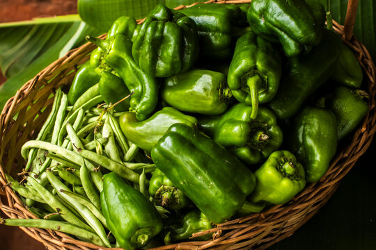 High-angle shot of a rustic wicker basket filled with fresh, organic green bell peppers and crisp green beans. 