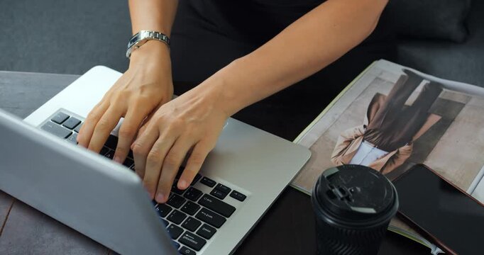 Hands typing on laptop keyboard for editing and proofreading, cup and magazine nearby, closeup captures deliberate keystrokes and precise corrections during content review session in calm studio