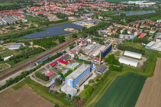Aerial view of an industrial complex featuring factory buildings, a railway line, a solar farm, and surrounding agricultural fields in Slavkov u Brna, South Moravian Region, Czechia.