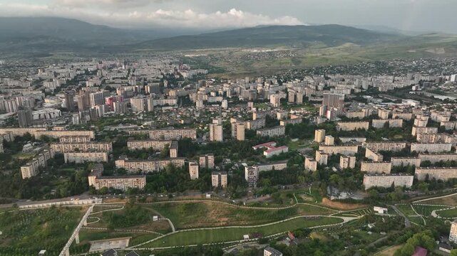 A high-angle aerial drone shot overlooking the dense residential microdistricts of Tbilisi, Georgia. The video frame showcases a vast urban landscape transition from Soviet-era panel apartment blocks 