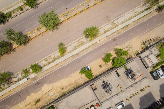 Aerial view of a multi-lane road with a sidewalk, green trees, and modern buildings in Greater Noida, Uttar Pradesh, India.