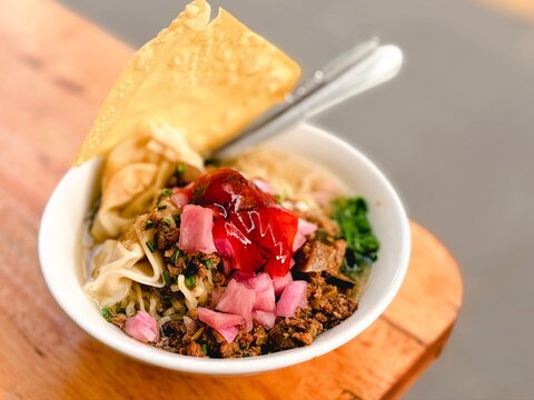 Delicious Asian Chicken Noodle Bowl with Minced Meat, Pickles, Vegetables, and Crispy Fried Wonton on Wooden Table