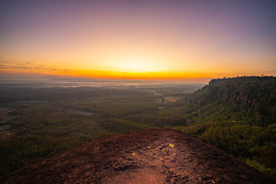 Silhouetted travelers gather on the massive rock formation of Three Whale Rock, watching the first light of day spread across the misty countryside of northeastern Thailand.