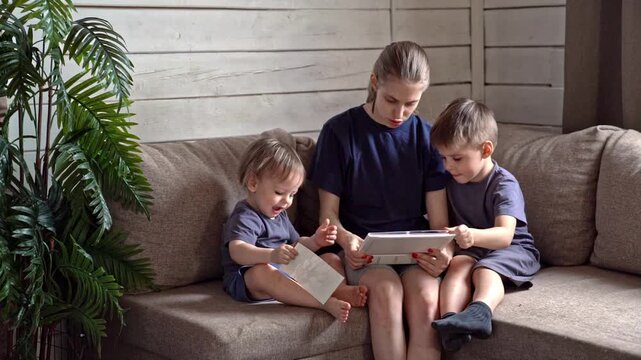 Young siblings engaging with books and digital devices at home. Children and their sibling collaboratively exploring knowledge through books and tablets in warm living room environment