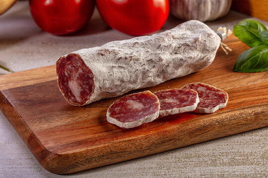 Sliced dry cured salami sausage on a wooden cutting board with fresh tomatoes, garlic, and basil. Traditional charcuterie appetizer