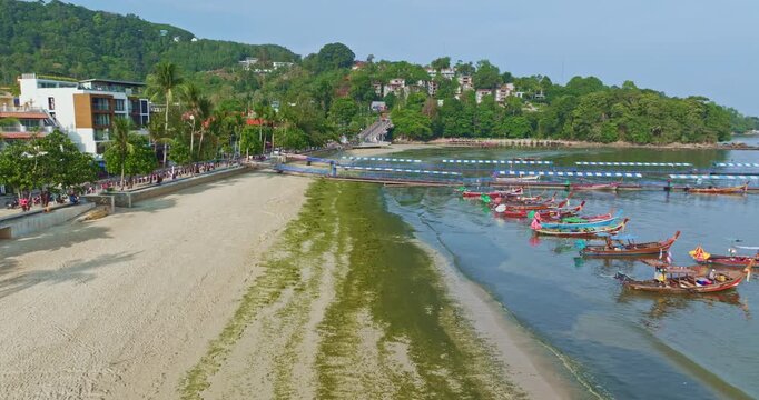 Top down aerial view of colorful fishing boats moored in shallow green water beside a sandy beach, with an excavator creating striking patterns on the shore. Environmental Cleanup on Sandy Beach