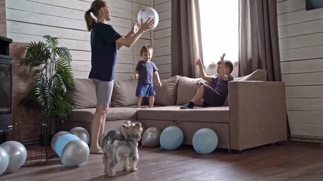 Woman leading symbolic balloon release indoors, teen caregiver and children perform quiet letting go ritual as balloons float, home plant and couch form intimate altar, contemplative mood and gentle