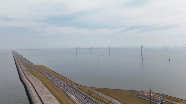 Aerial drone view of afsluitdijk causeway with cars driving and an offshore wind farm