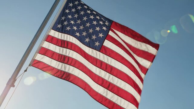 American flag waving in slow motion against blue sky with sun flare, celebrating patriotism, freedom, and national pride on independence day or memorial day celebration