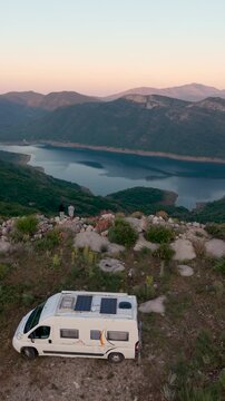 Montenegro. A couple experience stunning mountain vistas and the serene beauty of Bilecko jezero lake in Montenegro. Enjoy a peaceful holiday in a camper van while surrounded by nature during sunset.
