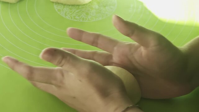 Baker hands actively kneading raw dough on a non-stick green silicone mat with measurement markings, showing the process of baking artisanal bread at home.