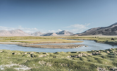 Clear-water rivers and lakes in a mountain valley, pastures and green grassy fields set against mountain ranges and snow-capped, glacier-clad peaks—a scenic landscape background © Denis