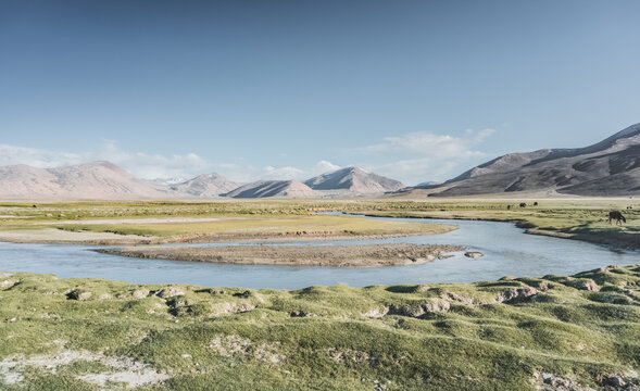 Clear-water rivers and lakes in a mountain valley, pastures and green grassy fields set against mountain ranges and snow-capped, glacier-clad peaks&mdash;a scenic landscape background