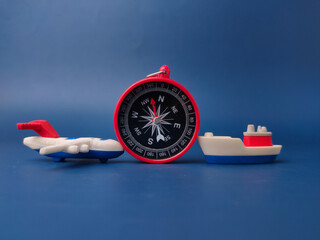 A red round compass is positioned between a small toy airplane and a toy cargo boat on a blue background © Mohd Azrin