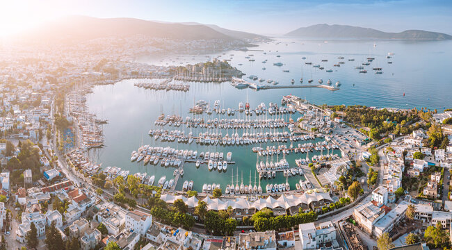 Aerial view of Bodrum, Turkey, showing the harbor filled with boats and yachts, and surrounding city buildings, under a warm sunset glow